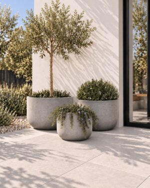 Set of three contemporary round Tube Planters in a natural grey finish, displayed in a modern outdoor courtyard.
