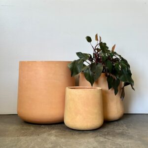 Set of three terracotta planters in minimalist design, natural earthy tones, perfect for indoor or outdoor plants, with one pot holding green foliage